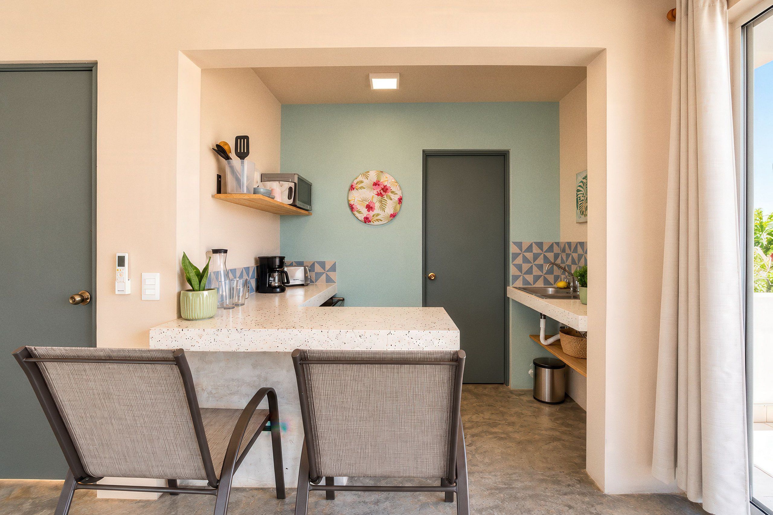 A compact kitchen with a central island, chairs, and a door leading to another room.
