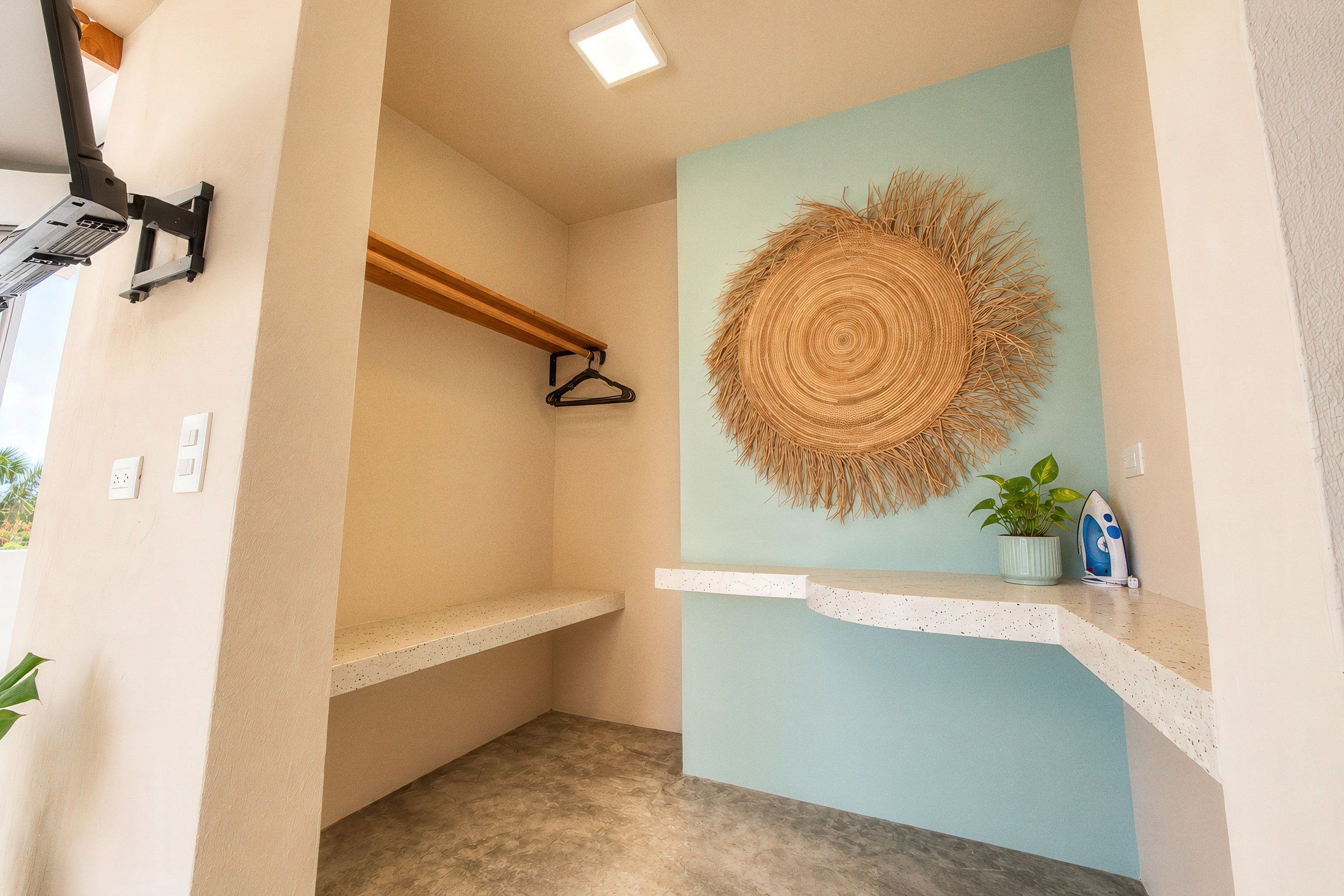 A bathroom with a towel rack, a hanging towel, a wall-mounted towel, and a small shelf with a plant and an iron.