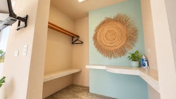 A bathroom with a towel rack, a hanging towel, a wall-mounted towel, and a small shelf with a plant and an iron.