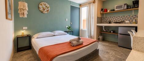 Een hotelkamer met een bed, nachtkastje, lamp en uitzicht op de keukenruimte.