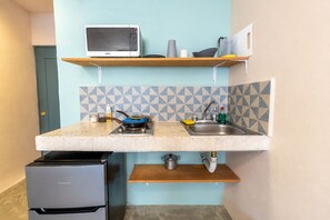 Una cocina compacta con microondas, un lavamanos, una hornilla y un refrigerador pequeño.