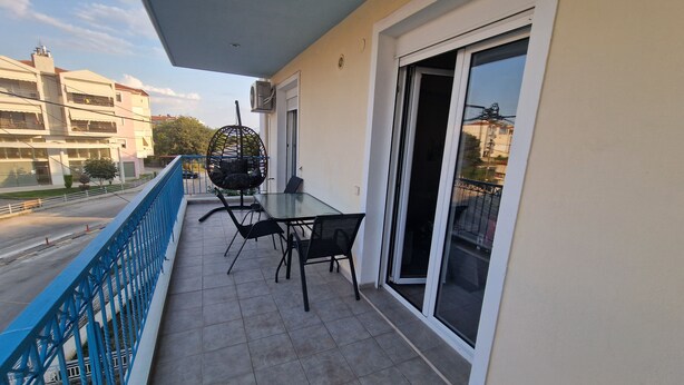 Ein Balkon mit Tisch und Stühlen, einem Hängesessel und einer Schiebetür.