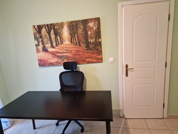 A room with a desk, a chair, a door, and a wall-mounted picture of a forest path.