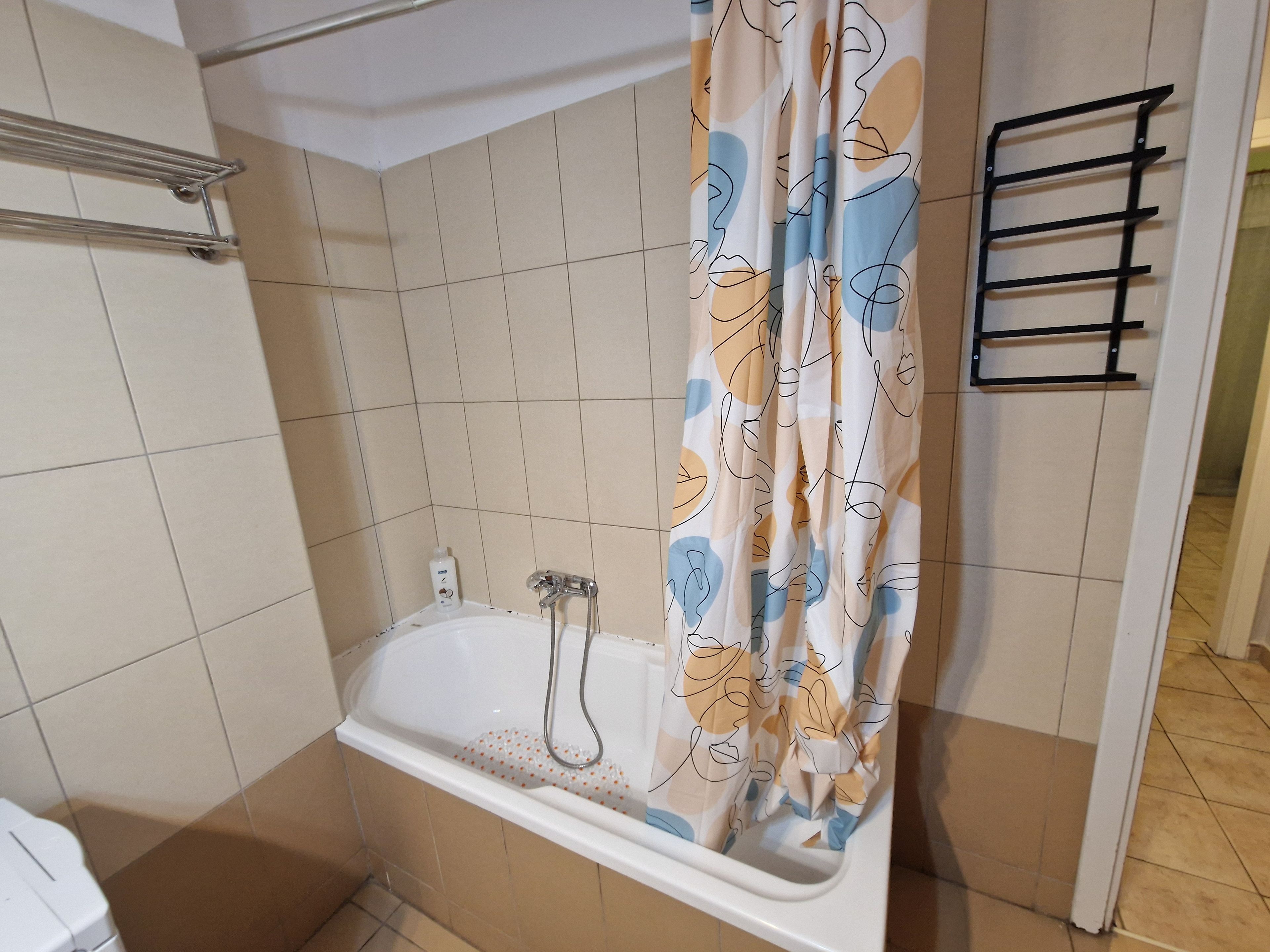 Un baño con una bañera, cortina de ducha, toallero y una botella de jabón de manos.