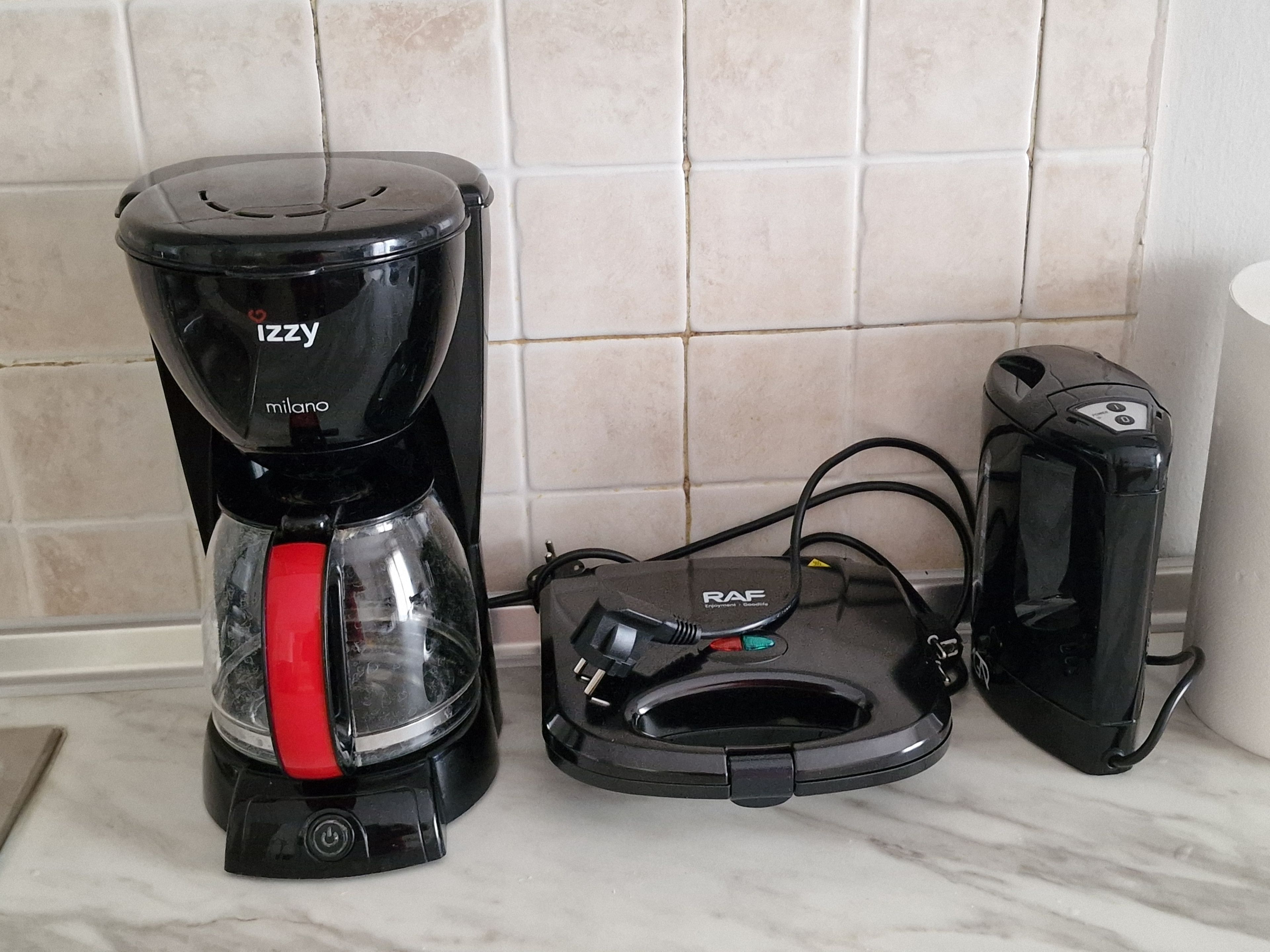 Una cafetera con asa roja, una regleta y un dispositivo negro con etiqueta blanca.