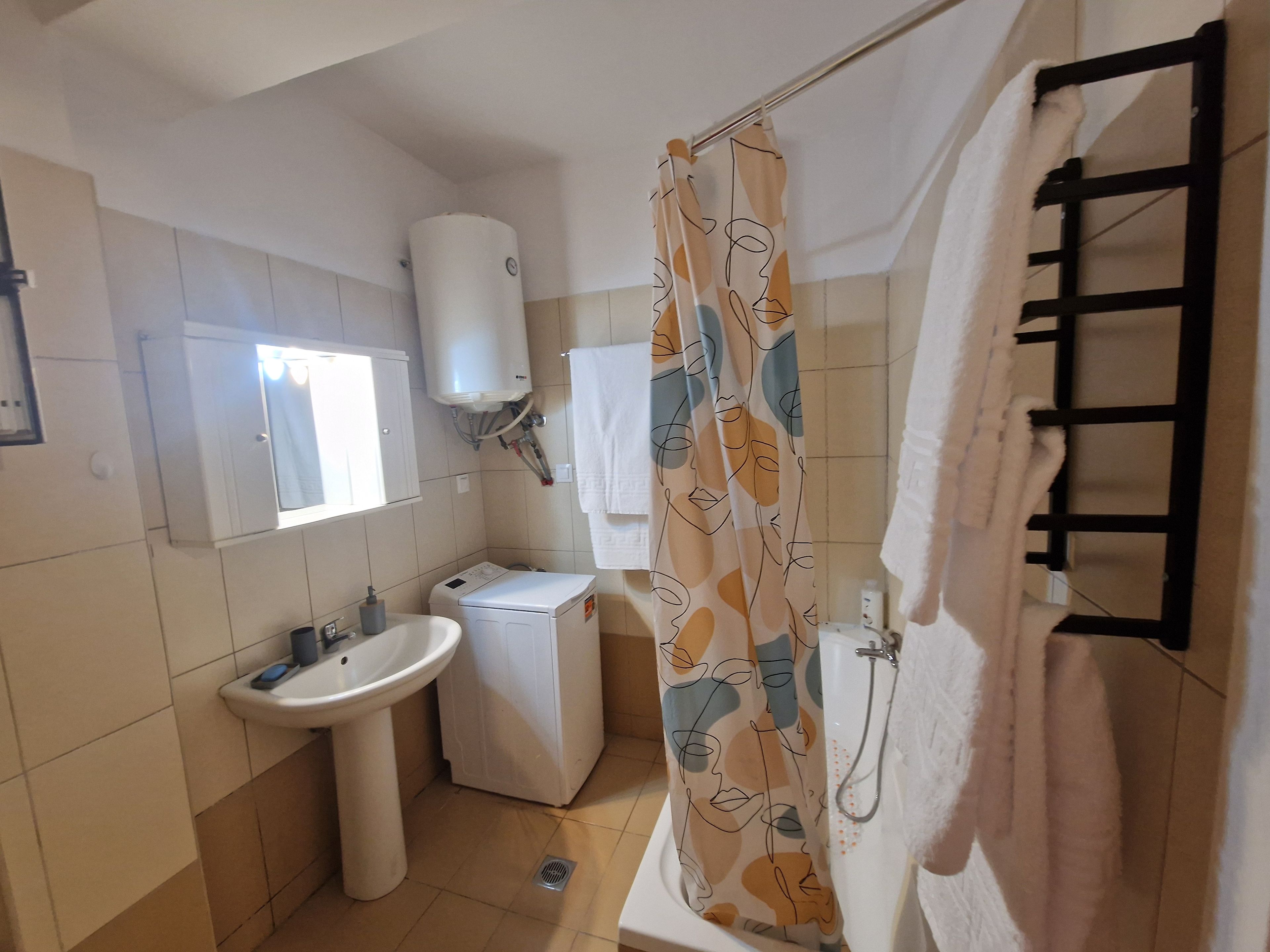 Un baño con lavamanos, inodoro, lavadora, toallero y cortina de ducha.