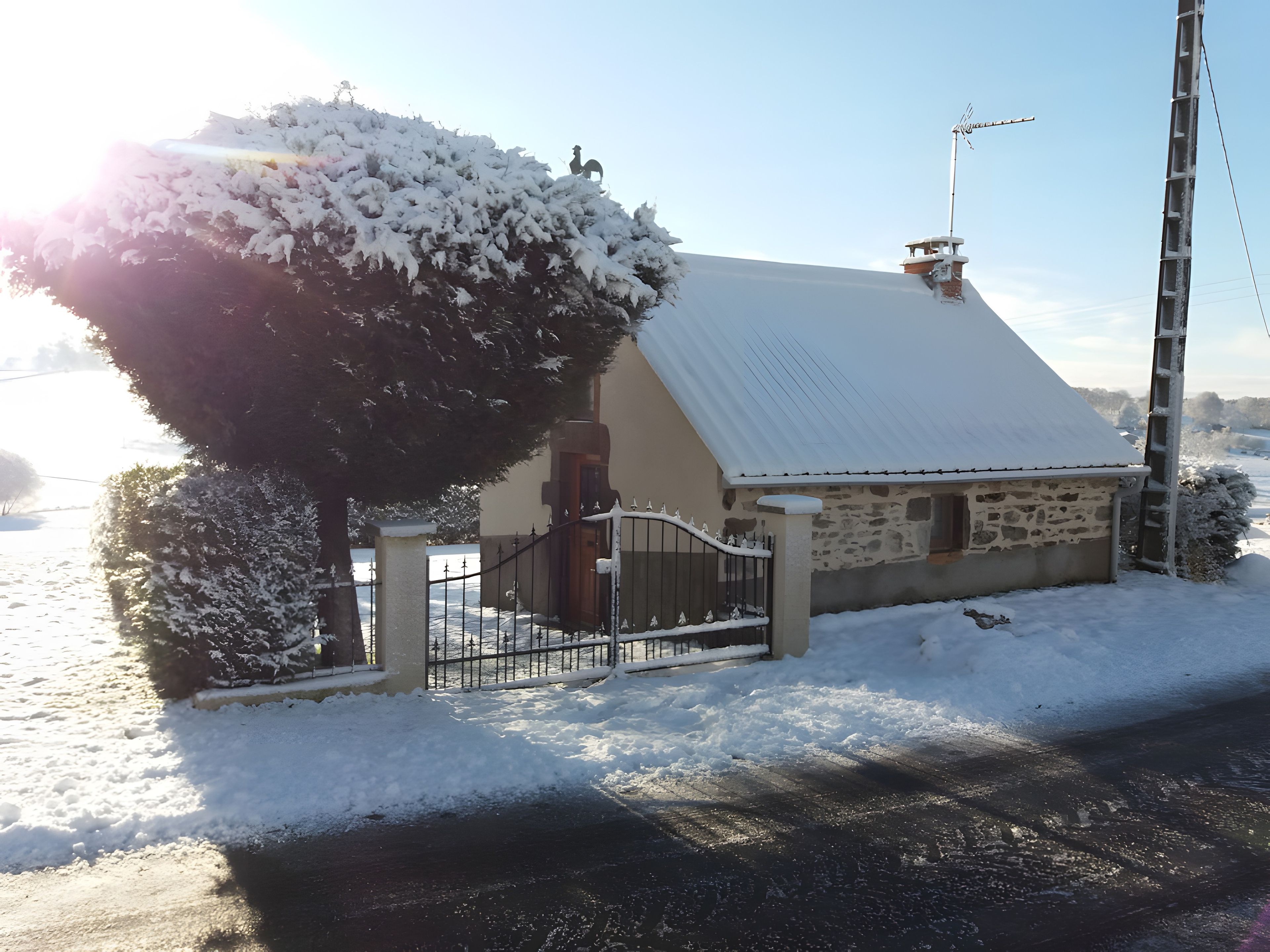 Une maison recouverte de neige, avec une façade en pierre, un portail en métal et une cheminée.