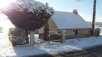 Une maison recouverte de neige, avec une façade en pierre, un portail en métal et une cheminée.