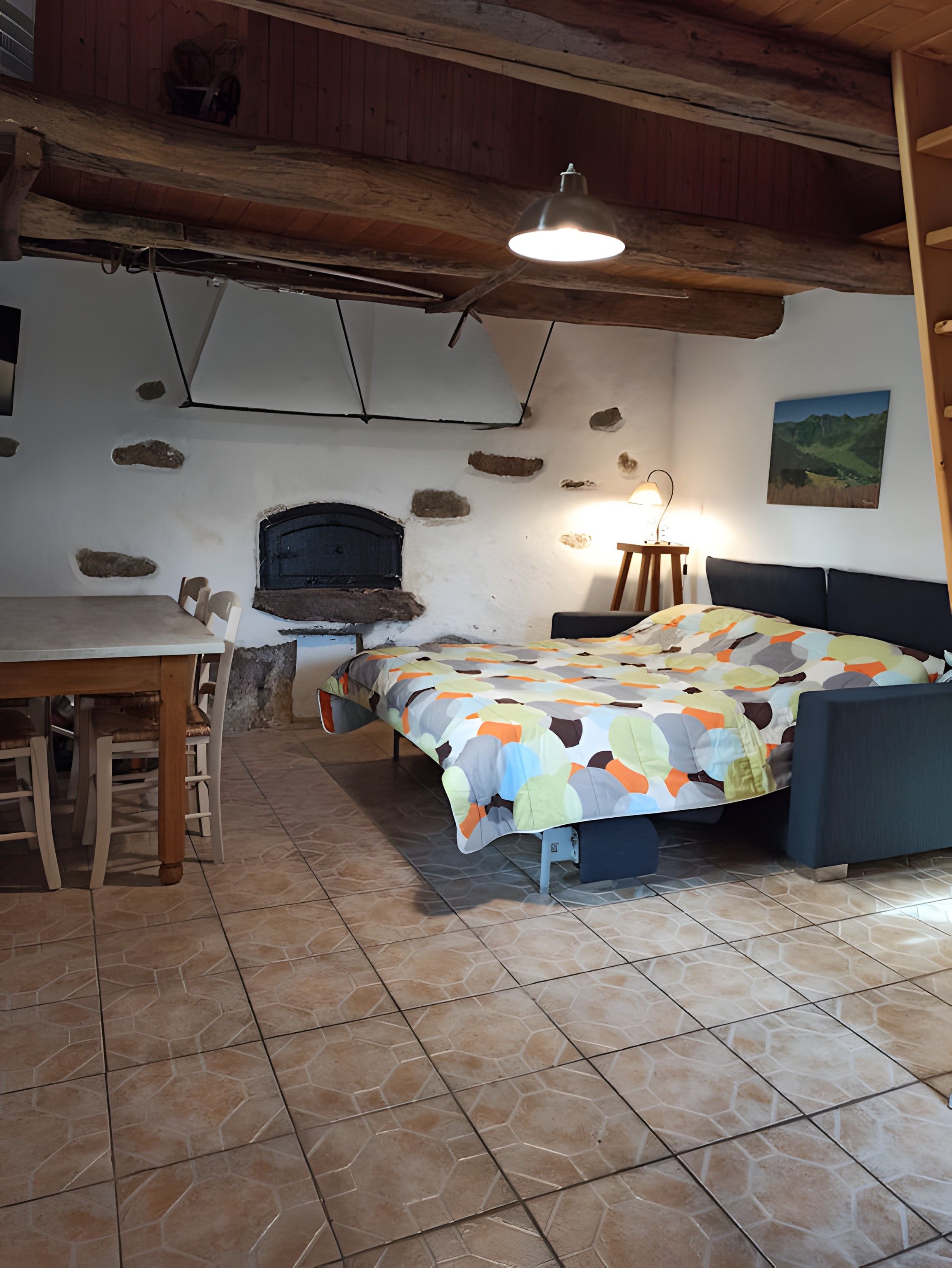 Een slaapkamer met een bed, een tafel, stoelen, een open haard en een schilderij aan de muur.