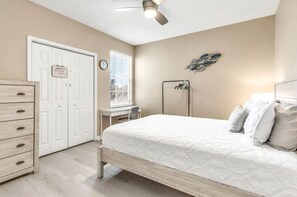 Ein Schlafzimmer mit einem Bett, einem Schreibtisch, einem Stuhl, einem Kleiderschrank und einem Deckenventilator.
