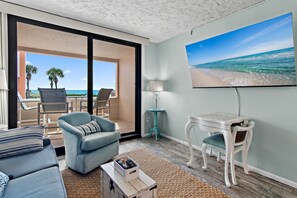 Una habitación con vista a la playa, un sofá, una silla, una mesita y un televisor en la pared.