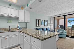 A modern kitchen with white cabinetry, granite countertops, and a dining area with a blue sofa and a view of the ocean. - 🌴Stunning Gulf Views | Pool | Jetty East 117A🌴 (Destin)