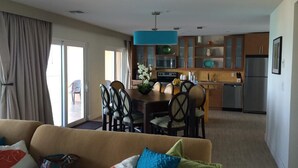 Una sala de estar con sofá, una zona de comedor con sillas y una mesa, y una cocina con armarios y electrodomésticos.