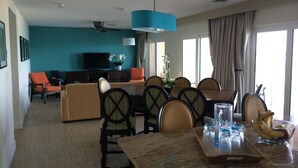 Una habitación de hotel con comedor, televisión y un amplio ventanal con cortinas.