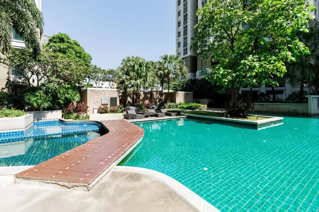 Une piscine dotée d’une terrasse carrelée, entourée de verdure et de bâtiments.