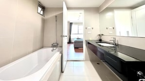 A modern bathroom with a bathtub, a large mirror, and a walk-in shower. - Belle Grand Rama 9 Bangkok (Krung Thep Maha Nakhon)