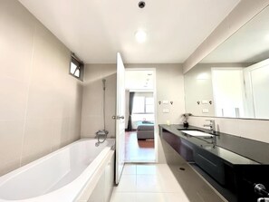 A modern bathroom with a bathtub, a large mirror, and a walk-in shower. - Belle Grand Rama 9 Bangkok (Krung Thep Maha Nakhon)