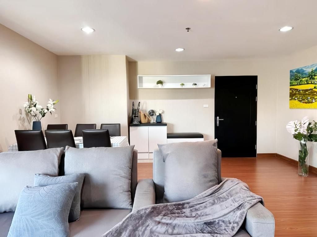 A modern living room with a sofa, a dining table with chairs, a kitchen area, and a door.