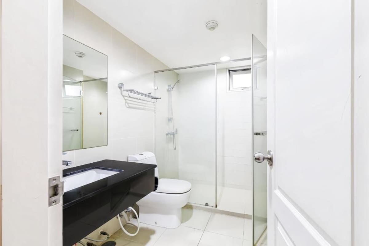 A modern bathroom with a glass shower enclosure, a white toilet, and a black sink.