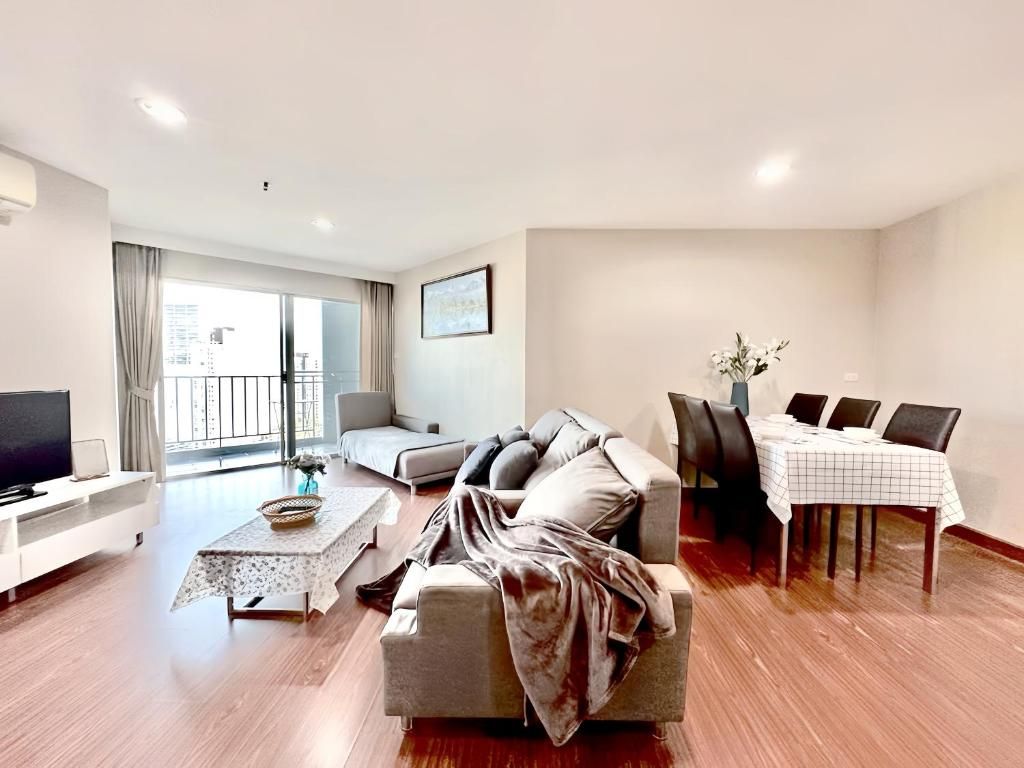 A modern living room with a sofa, a dining table with chairs, a television, and a balcony with curtains.