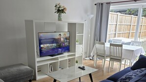 Una sala de estar con una televisión de pantalla plana, un sofá, una mesa de centro y un comedor con sillas.