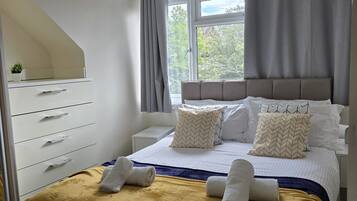 Un dormitorio moderno con una cama, una mesita de noche, un tocador y un armario, junto a una ventana con cortinas.