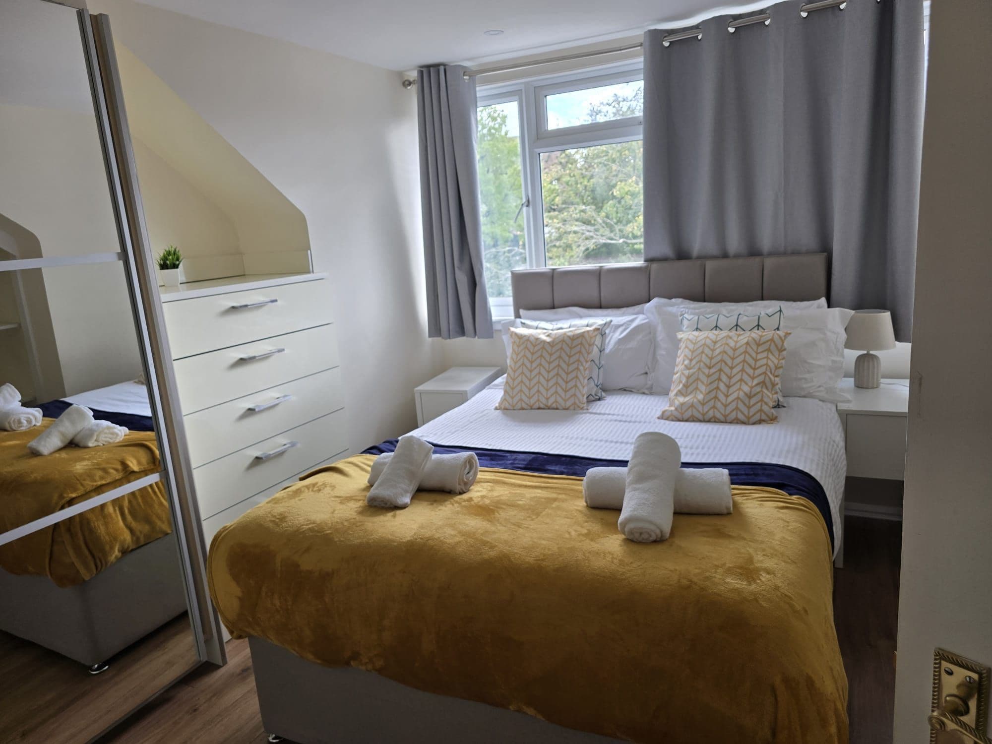 Una habitación de hotel con cama, mesita de noche, lámpara y espejo.