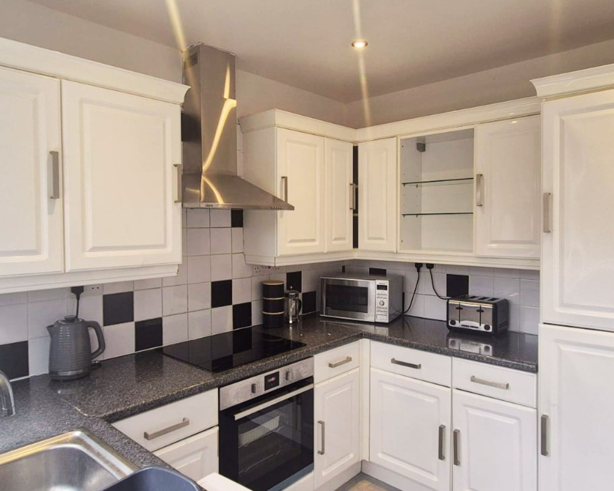 A modern kitchen with white cabinets, a black countertop, and stainless steel appliances including a microwave and oven.