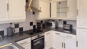 Una cocina moderna con gabinetes blancos, encimera negra y electrodomésticos de acero inoxidable, incluyendo un microondas y un horno.
