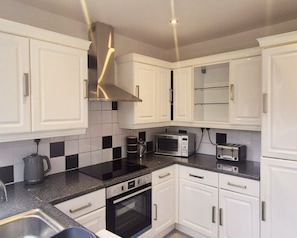 A modern kitchen with white cabinets, a black countertop, and stainless steel appliances including a microwave and oven. - Stylish 4BR Home in Essex | Sleeps 7 (South Benfleet)