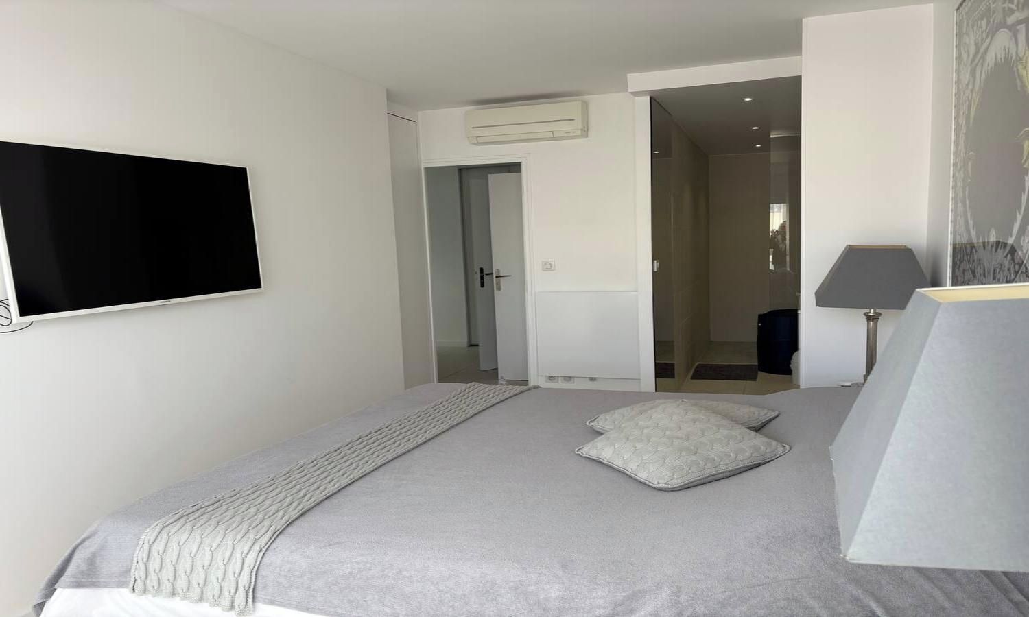 A bedroom with a bed, a television, a lamp, and a door leading to another room.