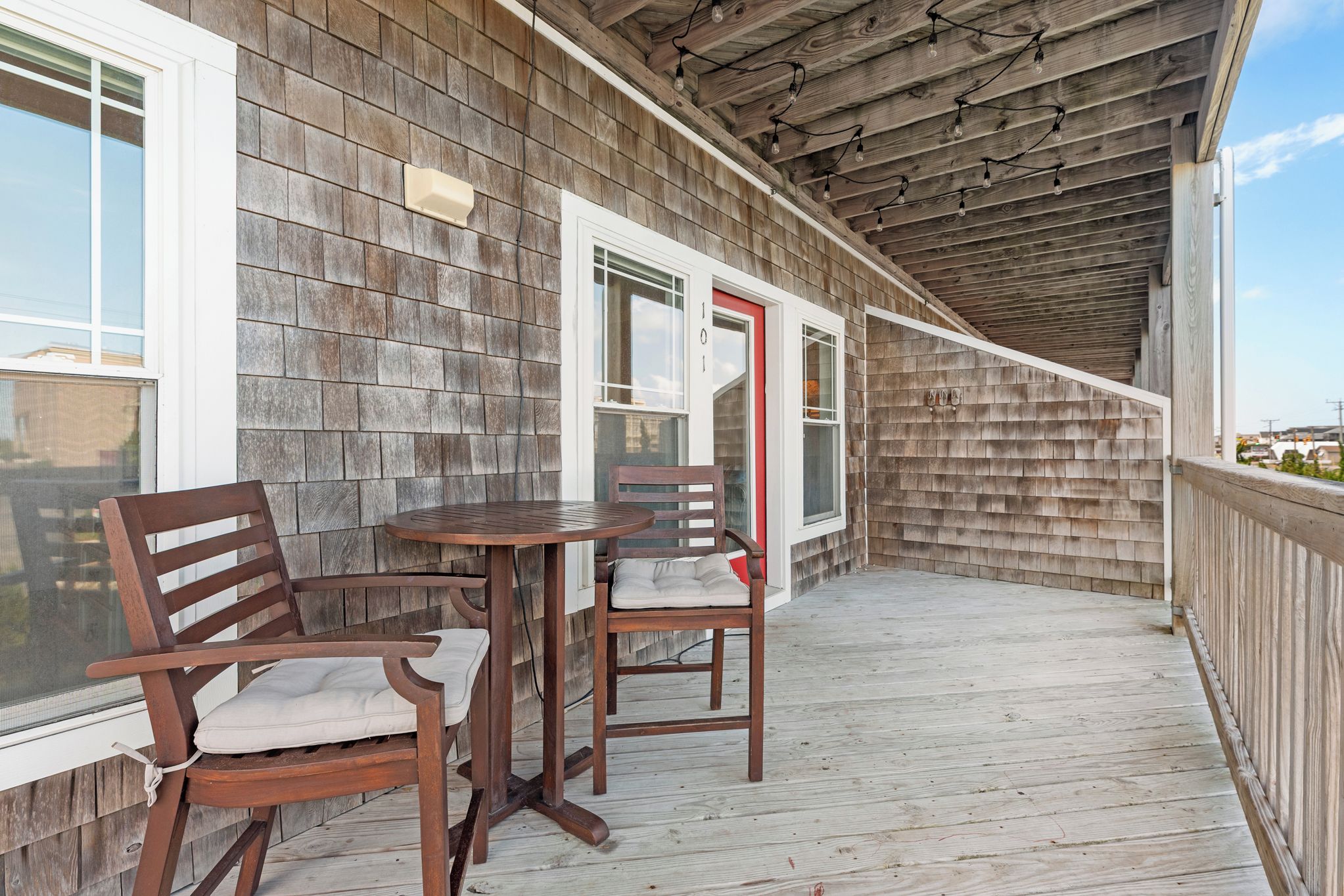 A wooden deck with a table and chairs, a red door, and a view of the sky.