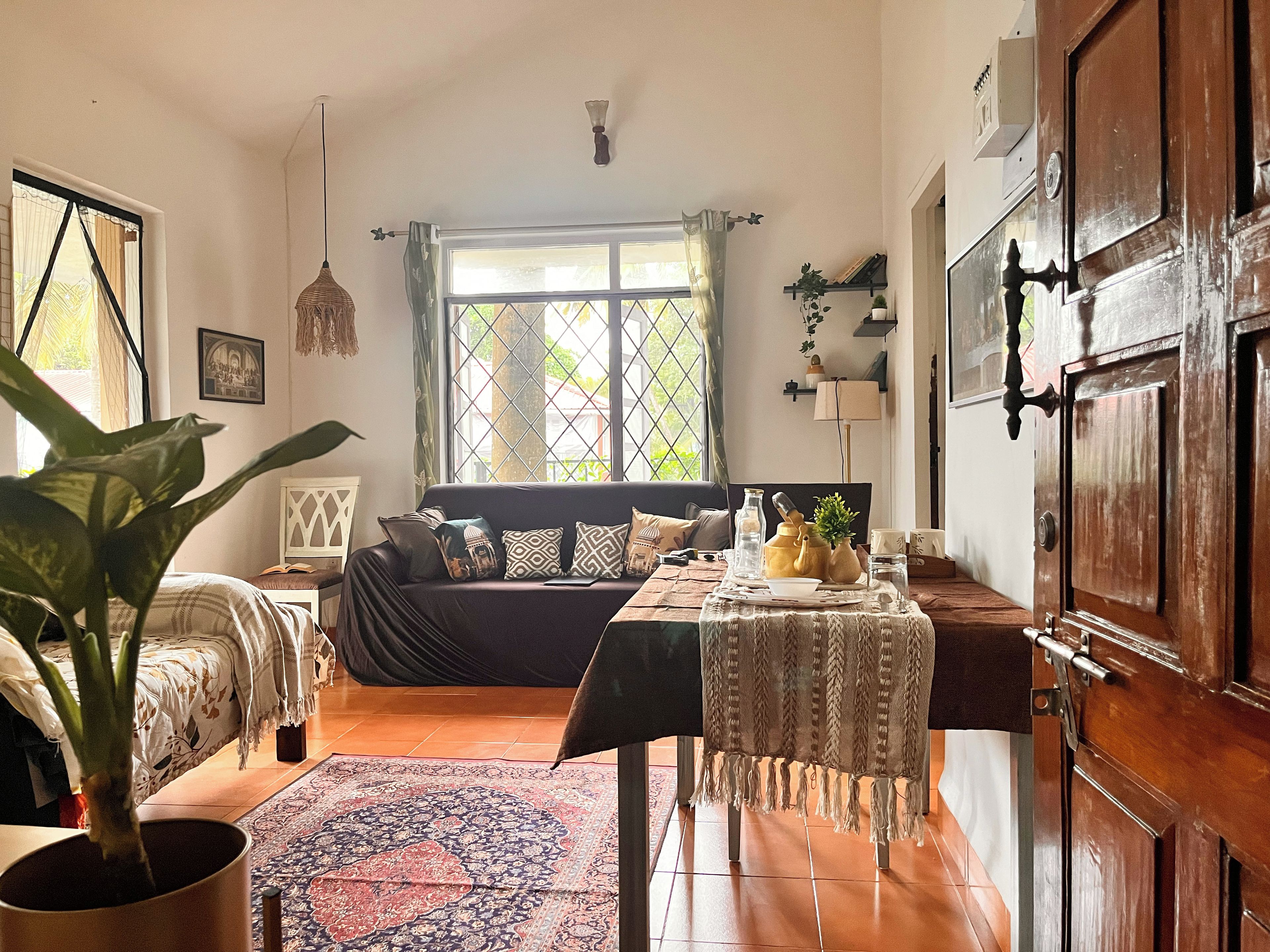 Una habitación acogedora con una cama, una mesa con adornos, una planta en maceta y una ventana con cortinas.
