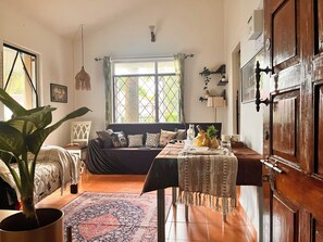 A cozy room with a bed, a table with decorative items, a potted plant, and a window with curtains. - 5 min walk to beach, 1 BHK Flat House in Candolim, fully equiped kitchen (Candolim)