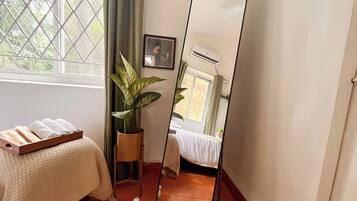 A room with a bed, a potted plant, a mirror, and a window with curtains.