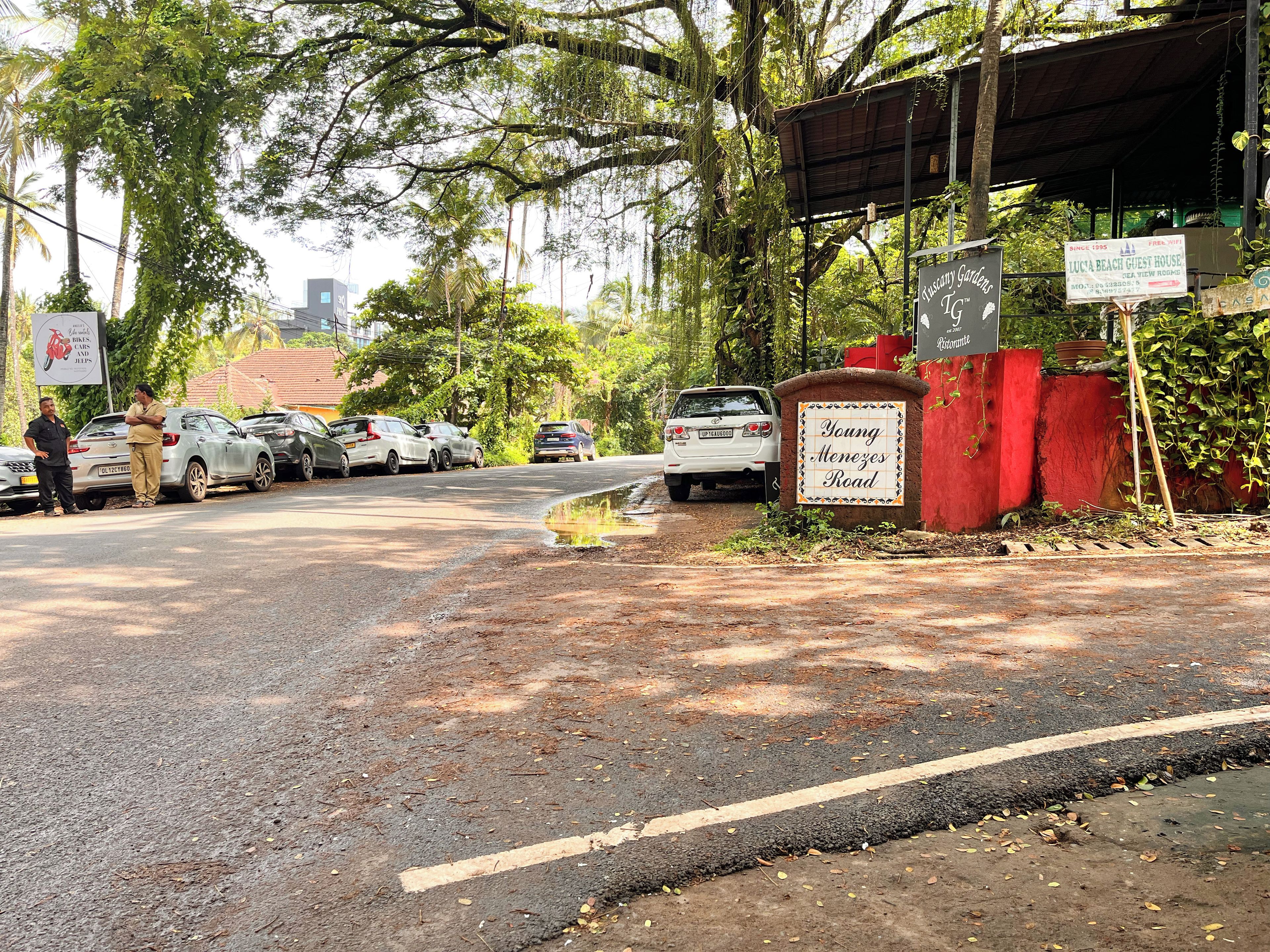 Eine Straße mit parkenden Autos und einem Schild für 'Young Menezos Road'.