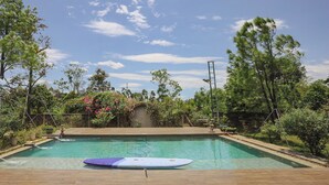 Une piscine avec une planche de surf, entourée d’arbres et sous un ciel dégagé.