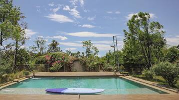 A swimming pool with a surfboard, surrounded by trees and a clear sky.