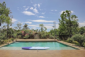 Piscina con una tabla de surf, rodeada de árboles y un cielo despejado.