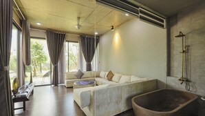 Une salle de bain moderne avec une baignoire sur pieds, une grande fenêtre avec des rideaux et un coin salon comprenant un canapé et une table ronde.