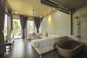 Un baño moderno con una bañera independiente, un ventanal grande con cortinas y un rincón de descanso con sofá y una mesa redonda.