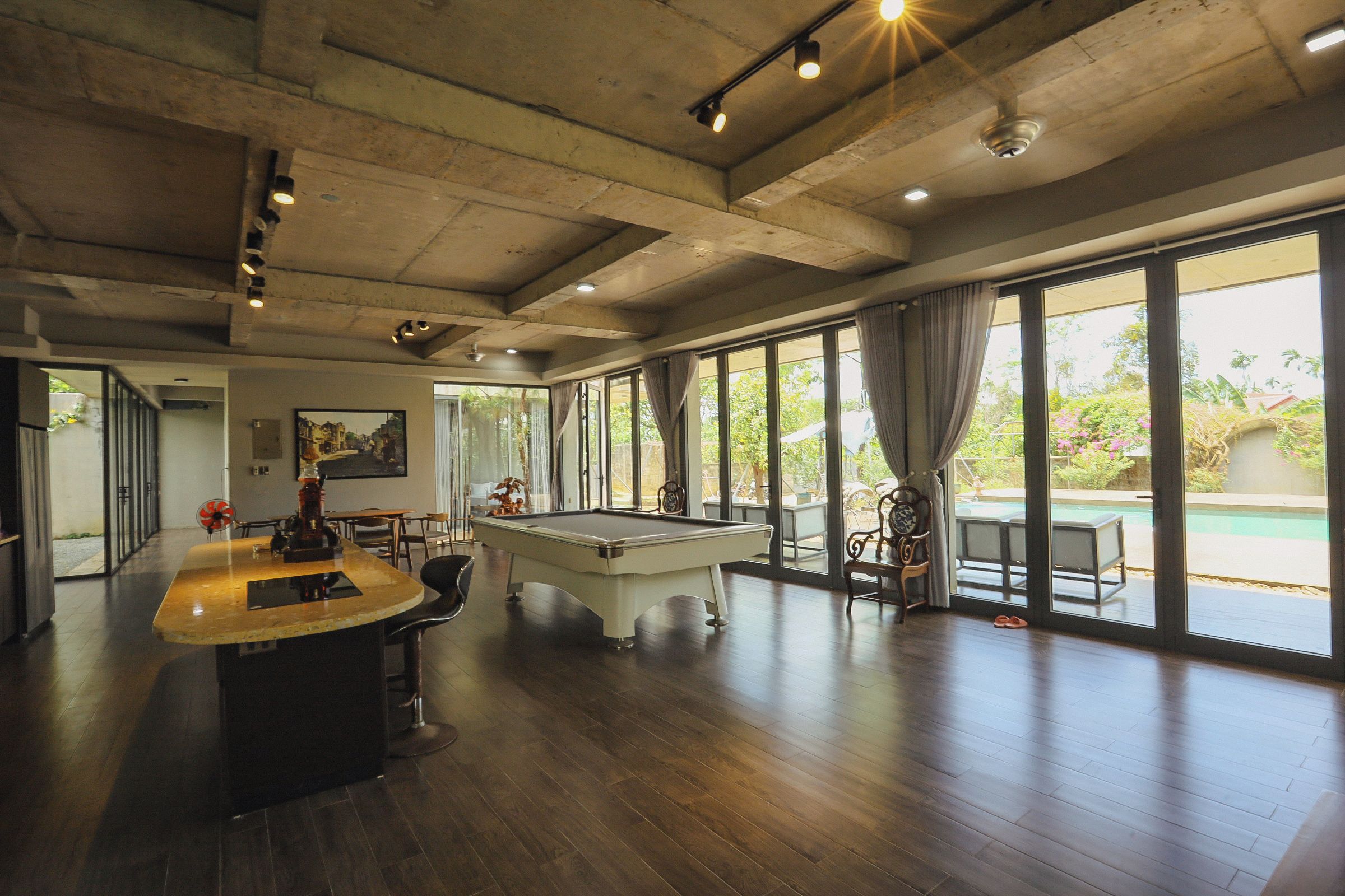 A spacious room with a pool table, a bar area, and large windows offering a view of the outdoors.