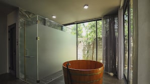 Une salle de bain moderne avec une douche à parois de verre, un lavabo en forme de tonneau en bois et une vue sur la verdure grâce à de grandes fenêtres.