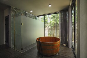 Un baño moderno con cabina de ducha de vidrio, lavamanos en forma de barril de madera y vistas a la vegetación a través de grandes ventanales.