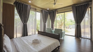 Une chambre d’hôtel avec un lit, un ventilateur de plafond et de grandes fenêtres équipées de rideaux.