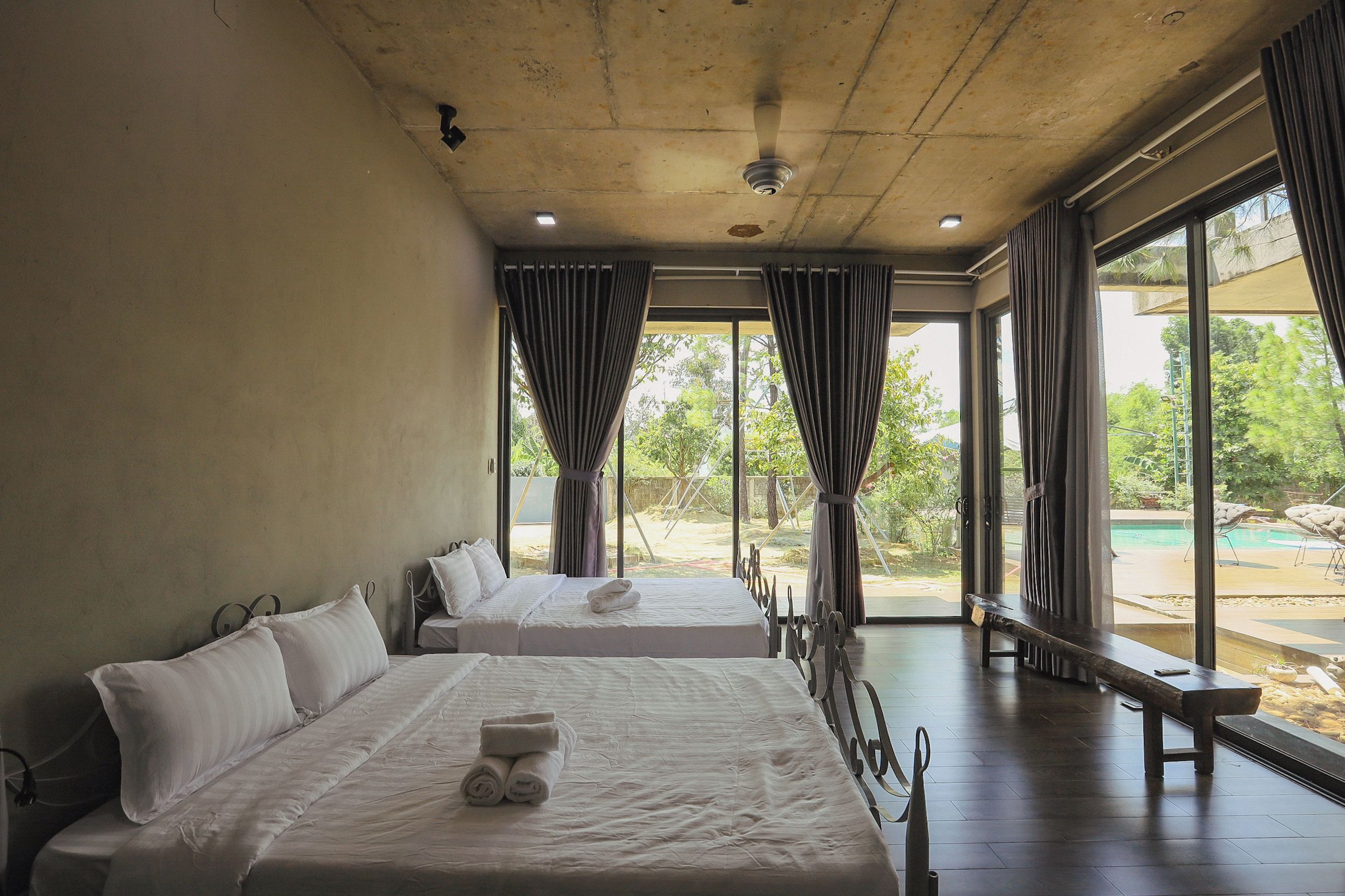 A hotel room with two beds, a bench, and a view of the outdoors.