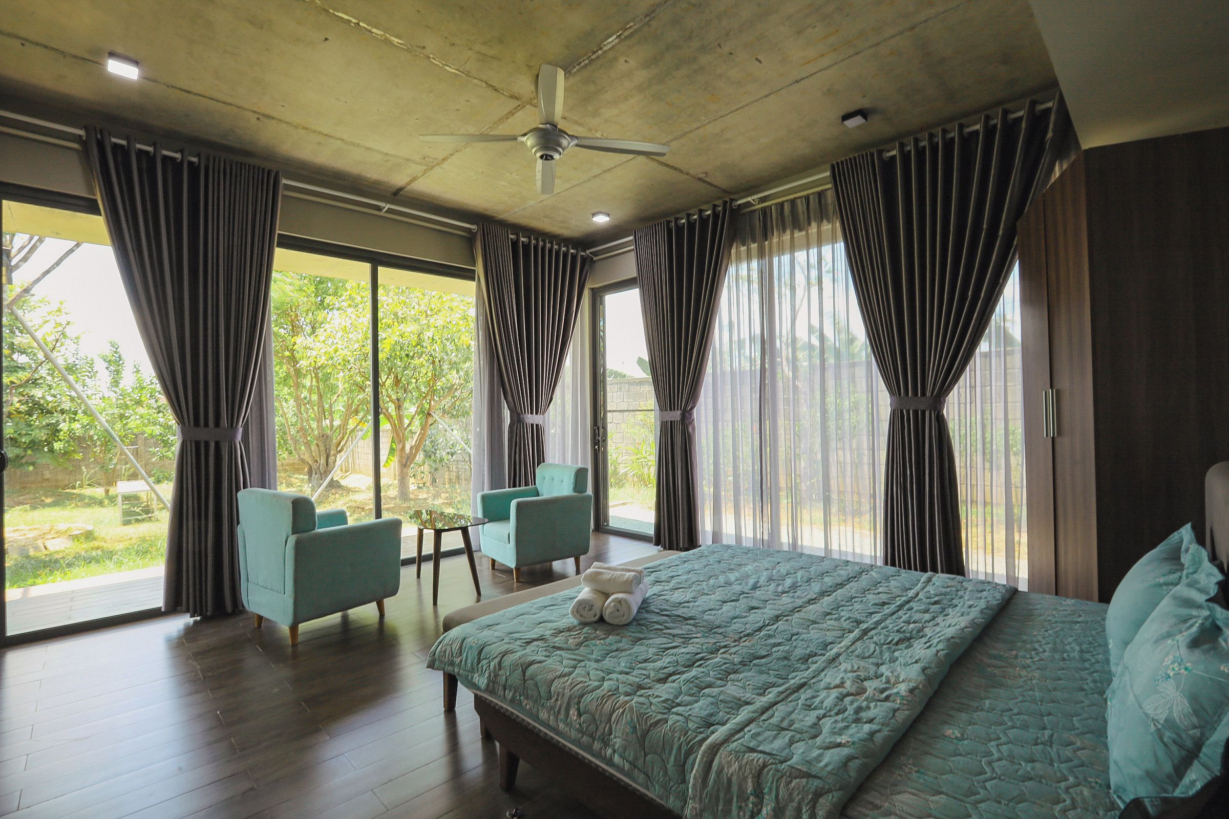 A bedroom with a large bed, two chairs, a small table, and a ceiling fan.