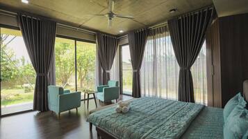 A bedroom with a large bed, two chairs, a small table, and a ceiling fan.
