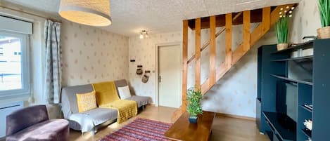 A living room with a sofa, armchair, wooden coffee table, and a staircase.