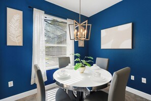 A dining area with a round table, chairs, a potted plant, and a wall-mounted light fixture. - Spacious 5-bedroom house in tranquil Kissimmee with AC (Kissimmee)